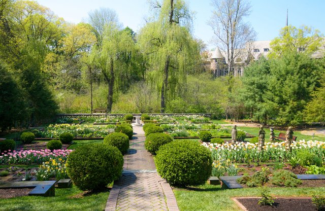 A garden full of flowers and topiary with a brick path through the center