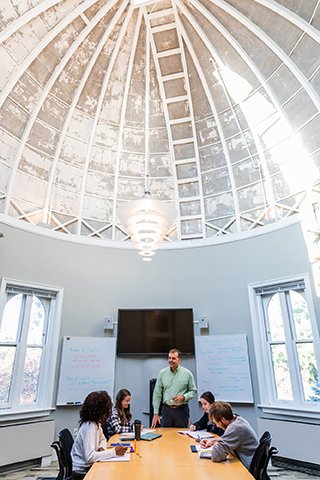 Four students and a professor sitting at a table in a room with a domed ceiling