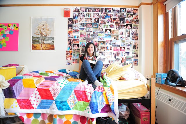 A student sitting on a colorful bed in a dorm room