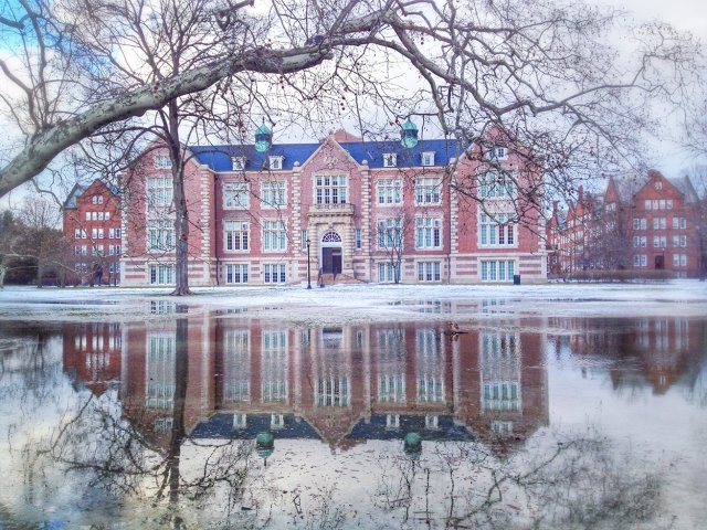A large, tan building surrounded by snow, reflected in ice on the ground
