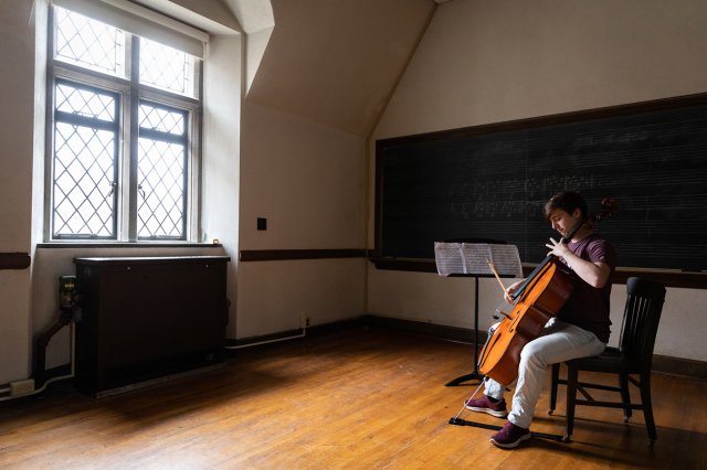 A student practicing cello in a classroom