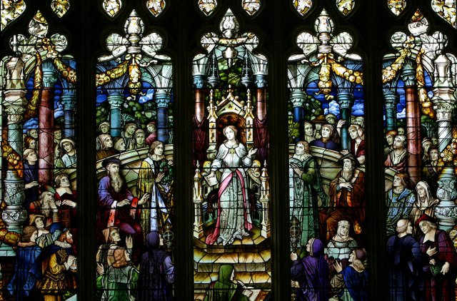 A stained glass window featuring a woman in a grey and pink dress