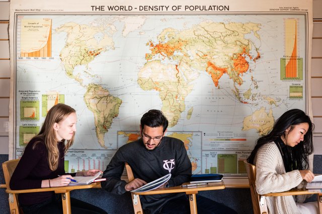 Three students sitting in a classroom with a large map on the wall in the background